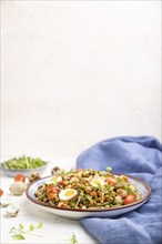 Mung bean porridge with quail eggs, tomatoes and microgreen sprouts on a white concrete background