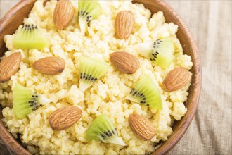 Millet porridge with kiwi and almonds in wooden bowl on a white wooden background and linen textile