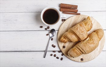 Two croissants with cup of coffee on wooden kitchen board on white wooden background. top view with