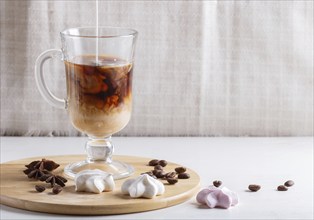 Glass cup of coffee with cream poured over and meringues on a wooden board on a white background.