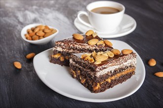 Chocolate cake with caramel, peanuts and almonds on a black wooden background. cup of coffee, close