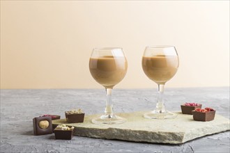 Sweet chocolate liqueur in glass with chocolate candies on a gray concrete background and stone