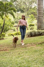 Vertical shot of a happy woman walking on the grass with her pet beside her outdoors. The woman is