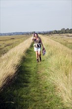 Woman walking flood defence bank, River Deben, Sutton, England, UK