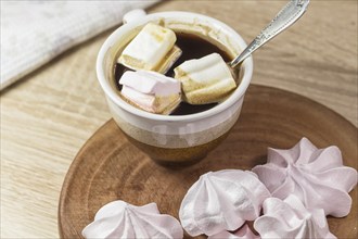 Chewing marshmallows, meringue and coffee cup on a wooden board and linen tablecloth