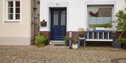 Bench and many flower pots in front of a house with entrance door and window in Warendorf,