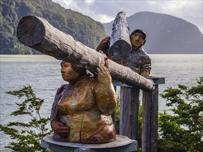 Sculputure of man and woman carrying trunks of a tree, seaside of Caleta Tortel, Caleta Tortel,