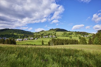 Landscape with hills, meadows, forests and a village under a blue sky with cumulus clouds near