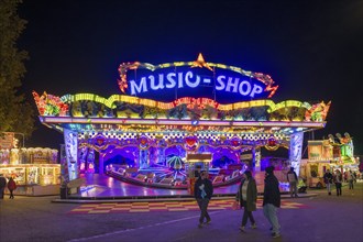 An illuminated carousel in the amusement park at night, surrounded by people and shining lights,