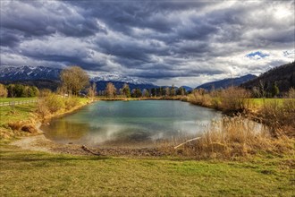 An idyllic pond against a mountain backdrop with a dramatic cloudy sky and autumnal vegetation,