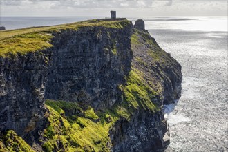 High cliffs on the horizon with an old tower surrounded by foaming sea, Cliffs of Moher