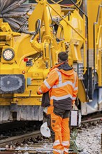 A worker in protective clothing operates a large yellow construction machine, track construction