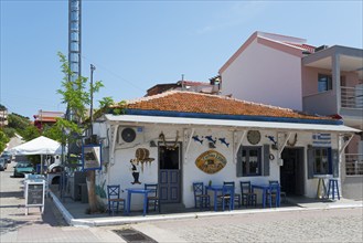 Rustic tavern on the corner with white facade, blue chairs and decorative elements surrounding,