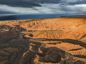 Riverbed runs through a landscape of eroded hills, badlands at sunset, Issyk Kul Lake in the