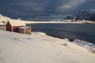 Cloudy mood with wooden hut by the sea in the snow, winter, mountains, Finnmark, Norway, Europe