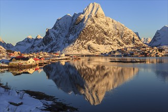 Snow-covered mountains reflected in fjord at sunrise, village, winter, Reine, Moskenesoya, Lofoten,