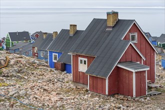 Colourful houses with black roofs stand on rocky ground near a grey coastline, fjord, remote Arctic