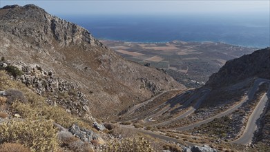 Panorama of a winding road that stretches through hilly terrain to the coast and the blue sea,