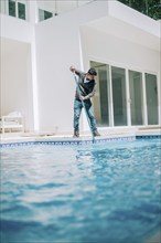 Maintenance person cleaning a beautiful home swimming pool. Worker cleaning a beautiful homemade