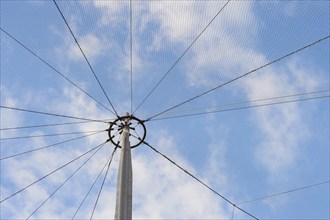 A pole with attached netting extends into a blue sky with scattered clouds, creating a geometric