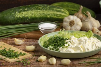 Fresh ingredients such as whole and grated cucumbers, garlic, chopped chives and sour cream on a