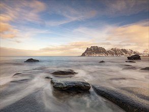 Smoothly polished rocks on Utakleiv beach in a dramatic cloudy atmosphere, snow-capped mountains in