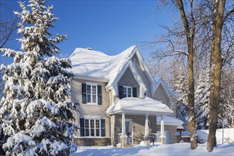 Country tan brick and vinyl cladded cottage style house facade with blue trim in winter, Quebec,