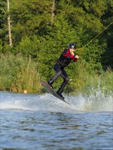 Young man jumping with wakeboard in lake, water sports, water skiing in wakepark