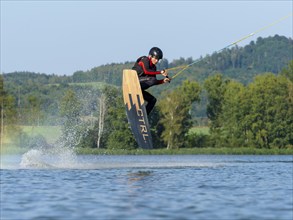 Young man jumping with wakeboard in lake, water sports, water skiing in wakepark, Stráž pod