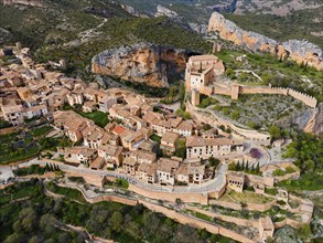 A picturesque village with tiled roofs and an impressive fortress surrounded by a mountainous