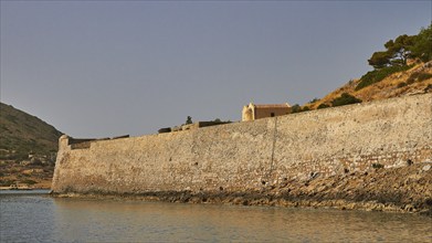 Long, old stone wall along the coastline, surrounded by a hill and calm sea, Venetian Sea Fortress,