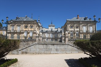 Baroque palace with symmetrical design and stone wall under a sunny sky, Royal Castle La Granja,