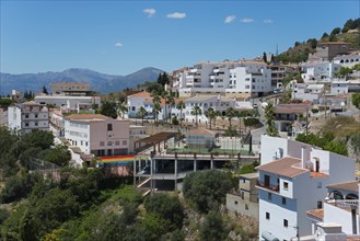 A panorama of a sunny village with white houses, orange-coloured roofs and green vegetation,