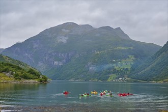 Several kayakers in a fjord surrounded by forested mountains and clouds, Geiranger, Geiranger