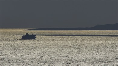 Silhouette of a ship on the glittering sea at sunset, calm evening mood, departure of the Bluestar