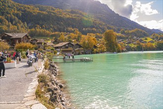 Picturesque lake with village, people on the shore and autumn trees in the background, Lake Brienz,