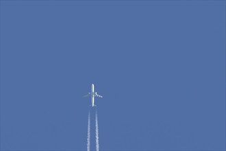 Boeing 777 aircraft flying across a blue sky leaving a contrail or vapor trail in the atmosphere