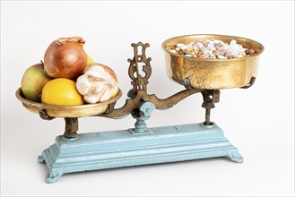 Kitchen scales with onions, garlic and fruit next to pills, white background