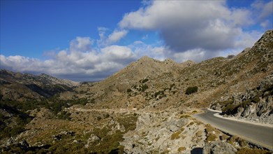 A lonely mountain path runs through a rough, stony landscape under a wide, clear sky, Kallikratis,