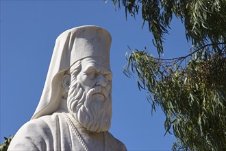 White bust of an othodox priest, A white statue of a bearded man in front of a clear blue sky, near