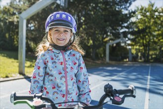 Girl with purple helmet smiles into the camera on a sunny sports field