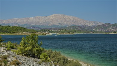 A lake with blue water, surrounded by green hills and mountains in clear, sunny weather, Gadouras