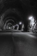 Dark illuminated tunnel with rough rock faces and an asphalted road, Zillertal, Austria, Germany,