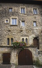 Old stone building facade with windows and decorated with colourful Pelargonium, Geranium flowers