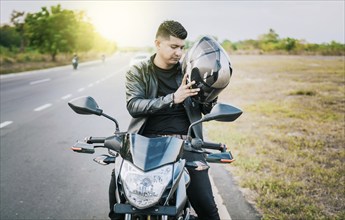 Young motorcyclist man putting on safety helmet outdoors. Male biker on motorcycle putting on