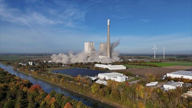 A power plant is being demolished, smoke rises, wind turbines stand next to it in an autumn