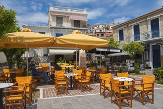 Street café with yellow parasols and wooden furniture in front of traditional buildings, Poros,