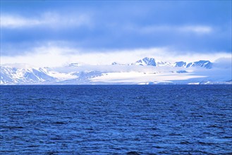 View in to land at Svalbard's rocky coast with snow capped mountains from the sea, Spitsbergen,