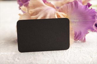 Black business card with iris purple flowers on white concrete background. side view, copy space,