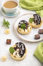 Sweet tartlets with chocolate and cheese cream with cup of coffee on a gray concrete background and